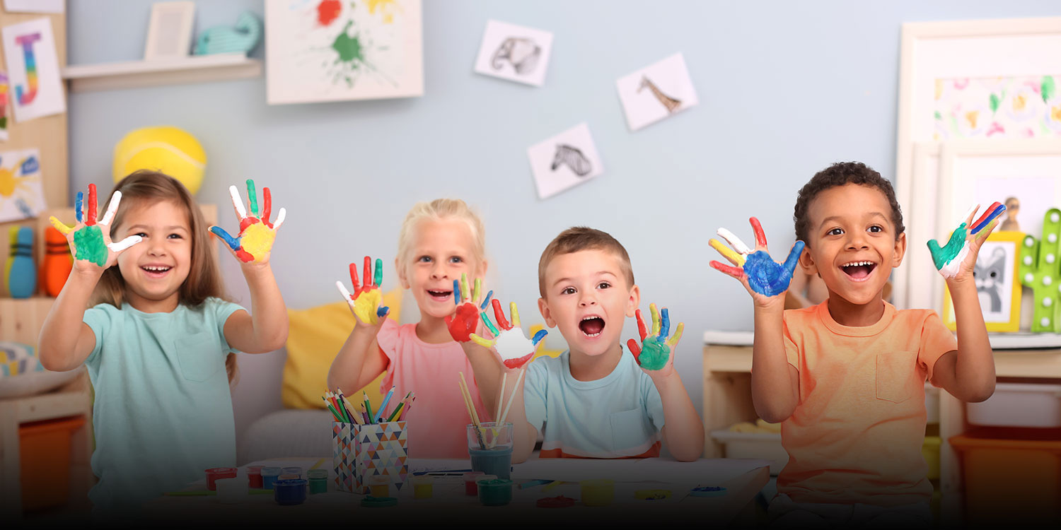 Smiling students holding up hands with finger paint.