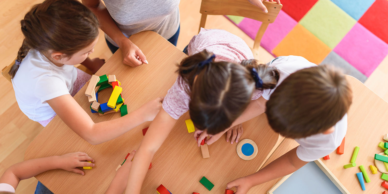 Overhead view of elementary students building with blocks at a table in a classroom.